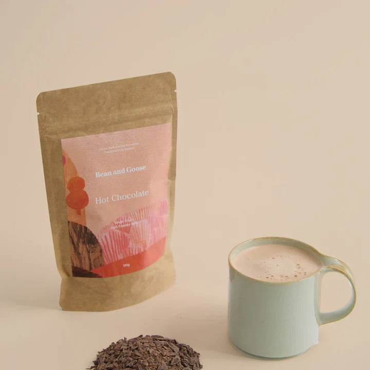A resealable pouch labeled 'Bean and Goose Hot Chocolate Pieces 120g' next to a mug of hot chocolate with visible steam.