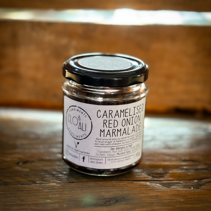 A jar of Caramelised Red Onion Marmalade with a label on the front, placed on a wooden surface with a wooden background.