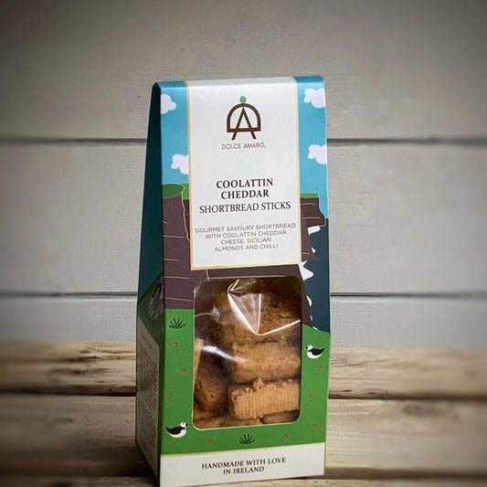 Packaged Dolce Amaro Coolattin Cheddar Shortbread Sticks on a wooden surface with a gray background