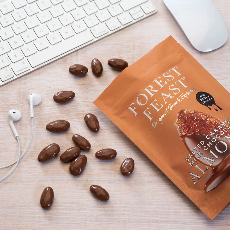 A bag of Forest Feast salted milk chocolate almonds on a marble surface, surrounded by loose almonds.