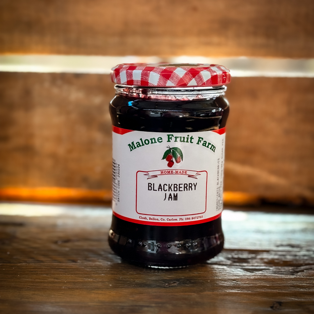 A jar of Malone's Fruit Farm blackberry jam with a red and white checkered pattern on the lid, placed on a wooden surface.