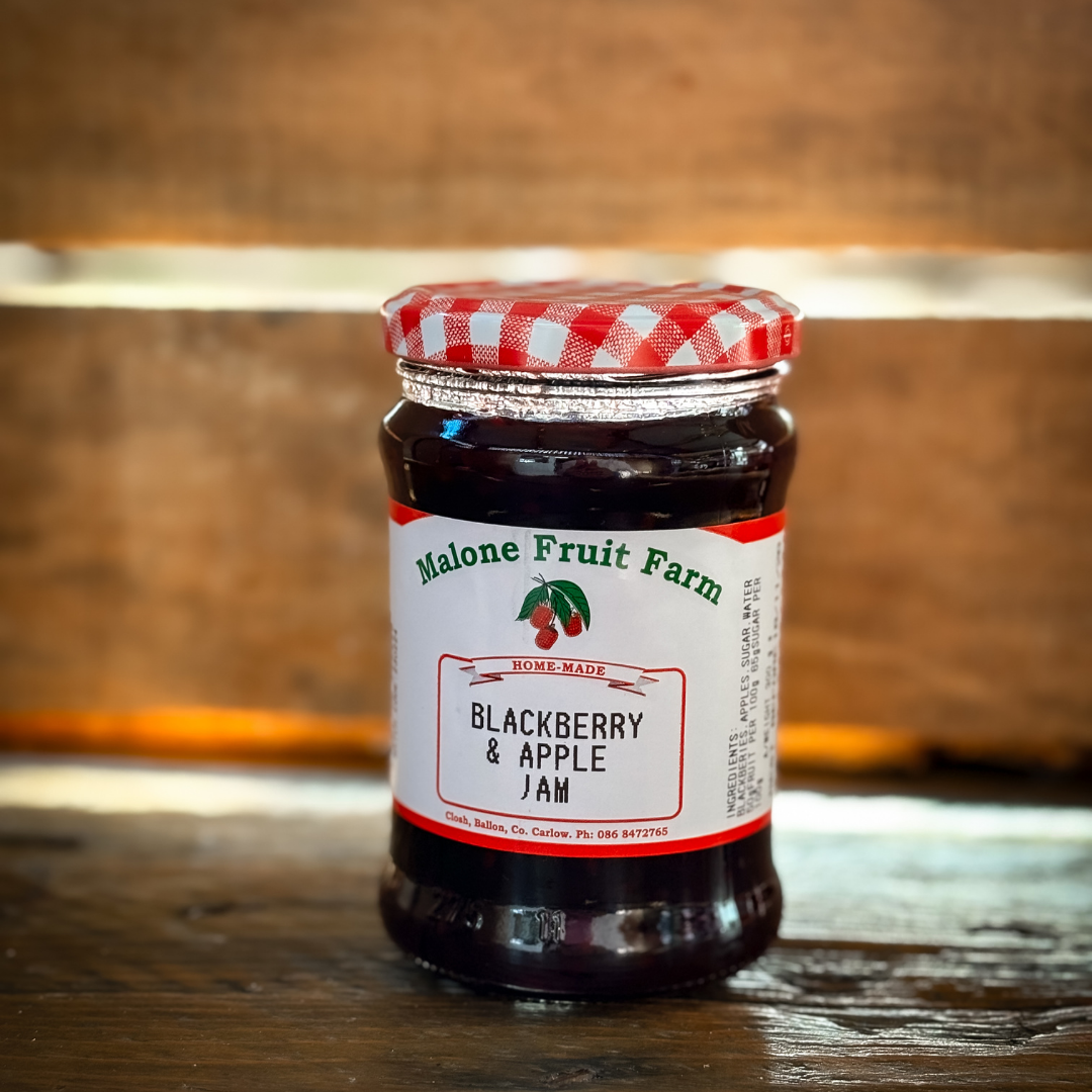 A jar of Malone's Fruit Farm blackberry and apple jam with a red and white checkered pattern on the lid, placed on a wooden surface.