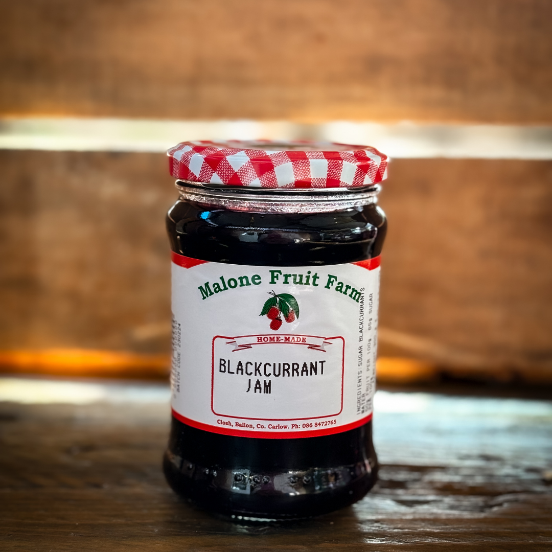 A jar of Malone's Fruit Farm blackcurrant jam with a red and white checkered pattern on the lid, placed on a wooden surface.