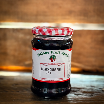 A jar of Malone's Fruit Farm blackcurrant jam with a red and white checkered pattern on the lid, placed on a wooden surface.