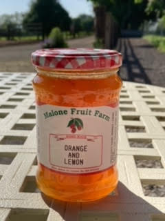 A jar of Malone's Fruit Farm orange and lemon marmalade with a red and white checkered pattern on the lid, placed on a white surface.