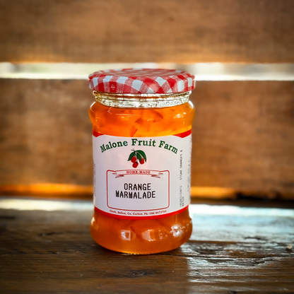 A jar of Malone's Fruit Farm orange marmalade with a red and white checkered pattern on the lid, placed on a wooden surface.