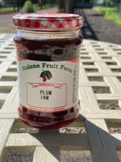 A jar of Malone's Fruit Farm plum jam with a red and white checkered pattern on the lid, placed on a white surface.
