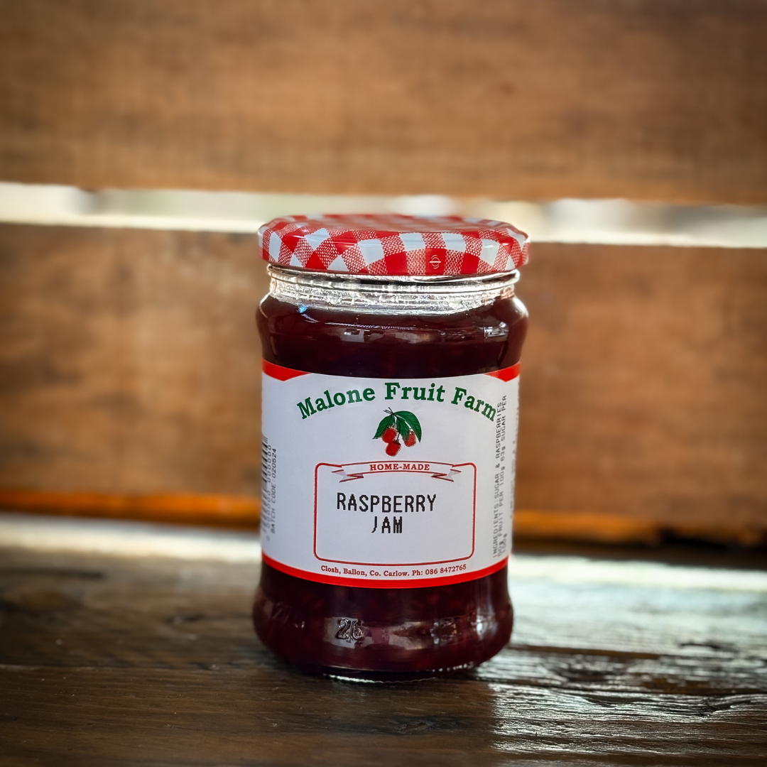 A jar of Malone's Fruit Farm Raspberry jam with a red and white checkered pattern on the lid, placed on a wooden surface.