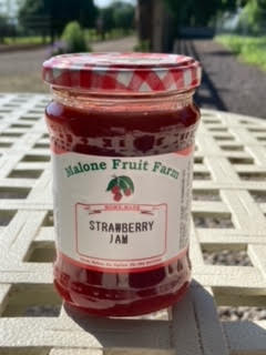 A jar of Malone's Fruit Farm strawberry jam with a red and white checkered pattern on the lid, placed on a white surface.