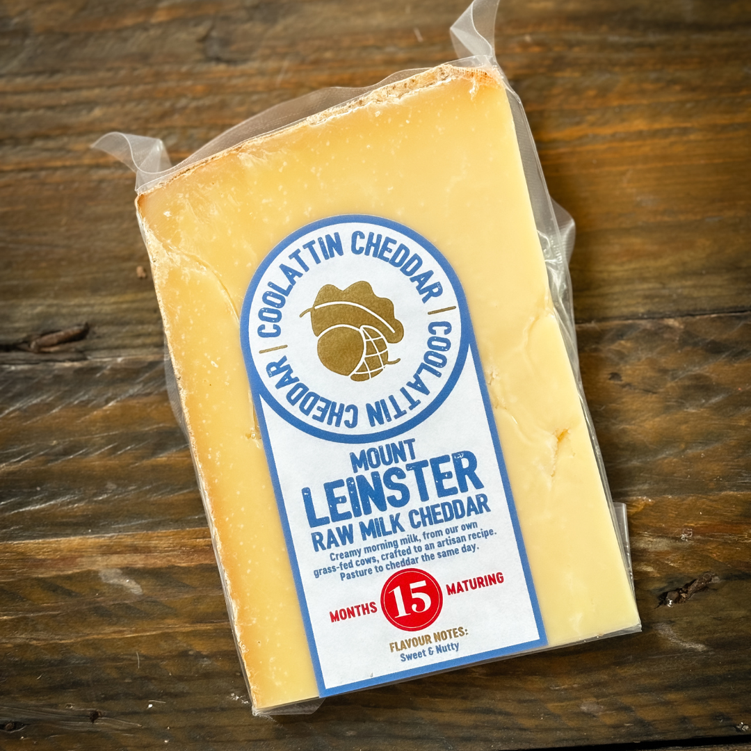 A packaged piece of Coolattin Mount Leinster Cheddar cheese on a wooden surface with a label indicating it is matured for 15 months