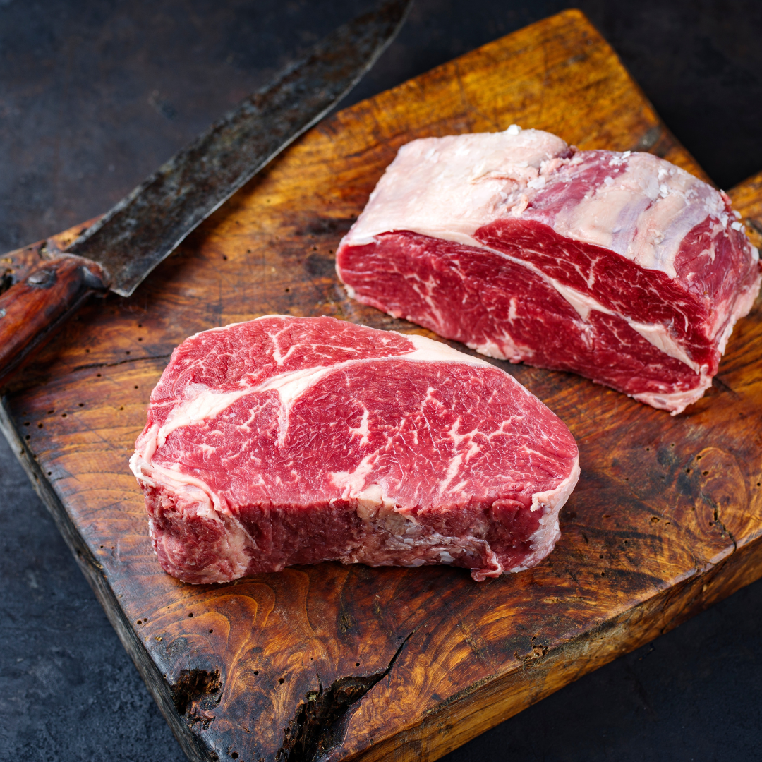 Several pieces of fresh, premium wagyu beef displayed on a wooden cutting board with a sharp knife to the side.
